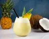 A piña colada cocktail is presented with a pineapple and a coconut in the background. Produktbild-Vorschau