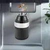 A garbage disposal unit installed under a sink, with food scraps in the sink drain. Produktbild-Vorschau
