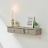 A floating shelf with two drawers mounted on a white wall, decorated with a candle, a picture frame, and a small plant. Voir les images du produit
