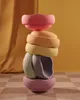 A stack of colorful, pastel-colored balancing stones on a checkered rug with a yellow curtain in the background. Anteprima dell’immagine prodotto