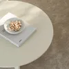 A close-up of a round, sand-colored side table with a book and a small bowl of pistachios on it. Voir les images du produit