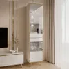 A tall, narrow white vitrine with gold accents and LED lighting, displayed in a modern living room setting. Produktbild-Vorschau