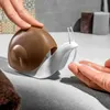 A person's hand is pressing down on a snail-shaped soap dispenser, dispensing soap into another hand. Voir les images du produit