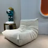 A large, plush, off-white beanbag chair is placed in a room with a gray wall, next to a small side table holding a decorative astronaut figurine. Produktbild-Vorschau