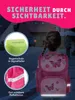 A young girl wearing a pink backpack with butterfly designs is walking on a street at dusk. The image highlights safety features of the backpack. Produktbild-Vorschau
