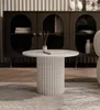 A round coffee table with a fluted base is placed on a rug in front of a dark cabinet. Voir les images du produit