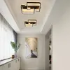 A hallway with two modern geometric ceiling lights, a large painting of an archway, and a cabinet with a vase and decorative items. Produktbild-Vorschau