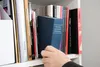 A hand is reaching for a blue book on a shelf filled with other books. Produktbild-Vorschau