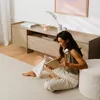 A woman is sitting on the floor reading a book in front of a TV stand. Produktbild-Vorschau