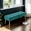 A tufted teal velvet bench with gold legs sits in a room with a dark teal wall and a window. Podgląd zdjęcia produktu