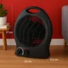A black electric heater is placed on a wooden floor in front of a red wall. A small plant in a white pot sits on a wooden side table to the left of the heater. Part of a gray sofa is visible on the right. Produktbild-Vorschau
