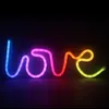 A neon sign spelling out the word "love" in rainbow colors against a black background. Anteprima dell’immagine prodotto
