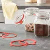 Several glass jars and red rubber seals are arranged on a gray countertop, with a yellow cloth in the background. Anteprima dell’immagine prodotto