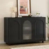 A black sideboard with arched doors and a fluted glass door is displayed in a room setting. Voir les images du produit