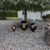 Three black globe-shaped garden lights are placed on a gravel path in front of a white house and under a tree. Produktbild-Vorschau