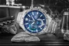A silver Casio Edifice watch with a blue face is displayed on a textured surface, with some rocks and a corkscrew in the background. Podgląd zdjęcia produktu