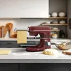 A red stand mixer with a pasta attachment is shown on a marble countertop, with a sheet of pasta emerging from the attachment. There is also a ball of dough and a rolling pin on the counter. Anteprima dell’immagine prodotto