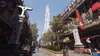 A street scene with buildings adorned with banners, a tall skyscraper in the distance, and trees. Produktbild-Vorschau