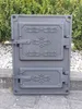 A cast iron stove door with decorative elements, placed outdoors on a stone surface with greenery in the background. Náhľad obrázku produktu
