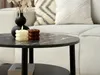 A close-up of a round coffee table with candles and a vase, with a couch in the background. Produktbild-Vorschau