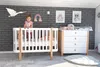 A baby is standing in a crib next to a changing table in a nursery. Produktbild-Vorschau