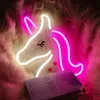 A neon unicorn light is displayed on a fluffy pink and white background, with a book and perfume bottle in the foreground. Náhled obrázku produktu