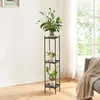A black metal plant stand with three shelves, holding potted plants and a vase with flowers, in a well-lit room with a window and a sofa in the background. Voir les images du produit