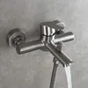 A close-up shot of a brushed nickel bathroom faucet mounted on a gray tiled wall, with water flowing from the spout. Produktbild-Vorschau