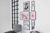 A collection of framed art prints displayed on a white wall next to a large window with black mullions. A chair with a knitted cushion is in the foreground. Produktbild-Vorschau