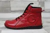 A red leather boot with black laces and sole, set against a light gray and white wood-plank background. Produktbild-Vorschau