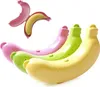 A group of banana-shaped storage containers in pink, green, and yellow, with one pink container open showing a banana inside. Produktbild-Vorschau