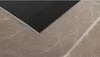 A close-up view of the edge of a black glass ceramic hob resting on a marble countertop. Produktbild-Vorschau
