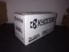 A cardboard box for a Kyocera toner cartridge sits on a dark surface. Náhľad obrázku produktu