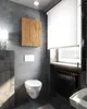 A modern bathroom with concrete-look walls, a wall-mounted toilet, a wooden cabinet, and a radiator under a window with blinds. Voir les images du produit