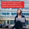 A woman sits outdoors with a laptop, with a building in the background. Produktbild-Vorschau