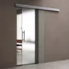 A modern frosted glass sliding door with a silver handle, installed in a room with a brown wall and concrete floor. Produktbild-Vorschau