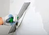 A gloved hand is using a trowel to apply white plaster to a wall. Produktbild-Vorschau