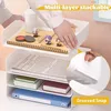 A person is stacking a white multi-layer desk organizer with various office supplies and books. Produktbild-Vorschau