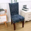 A chair with a blue leaf-patterned slipcover is shown in a room setting, next to a nightstand with books. Náhled obrázku produktu