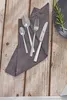 A set of cutlery laid out on a wooden table, with a grey napkin. Produktbild-Vorschau