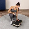 A woman in workout clothes is kneeling next to a vibration plate, holding a remote control. Náhľad obrázku produktu