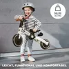 A young child wearing a helmet is holding a Kinderkraft 4TRIKE 3-in-1 balance bike/tricycle. The background is a concrete wall and floor. Produktbild-Vorschau