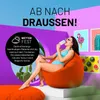 A woman in a bikini sits on an orange beanbag chair, eating an ice cream, with a tropical background and framed art. Voir les images du produit