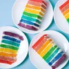 Slices of rainbow cake on white plates against a light blue background. Náhled obrázku produktu