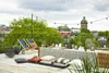A rooftop terrace set up for an outdoor gathering with string lights, a table set for dining, lounge chairs, and cushions. Náhled obrázku produktu