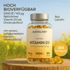 A bottle of Vitamin D3 softgels is placed on a wooden surface with a blurred background of yellow flowers. Produktbild-Vorschau