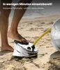 A person's foot is pressing down on a foot pump on a sandy beach, with a yellow hose connected to a silver object. Voir les images du produit