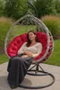 A woman is sleeping in a hanging egg chair outdoors. Produktbild-Vorschau