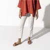 A person wearing an orange top and white pants, with Birkenstock sandals. Podgląd zdjęcia produktu