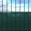 A green privacy screen is attached to a black metal fence, with a cloudy blue sky visible above. Podgląd zdjęcia produktu